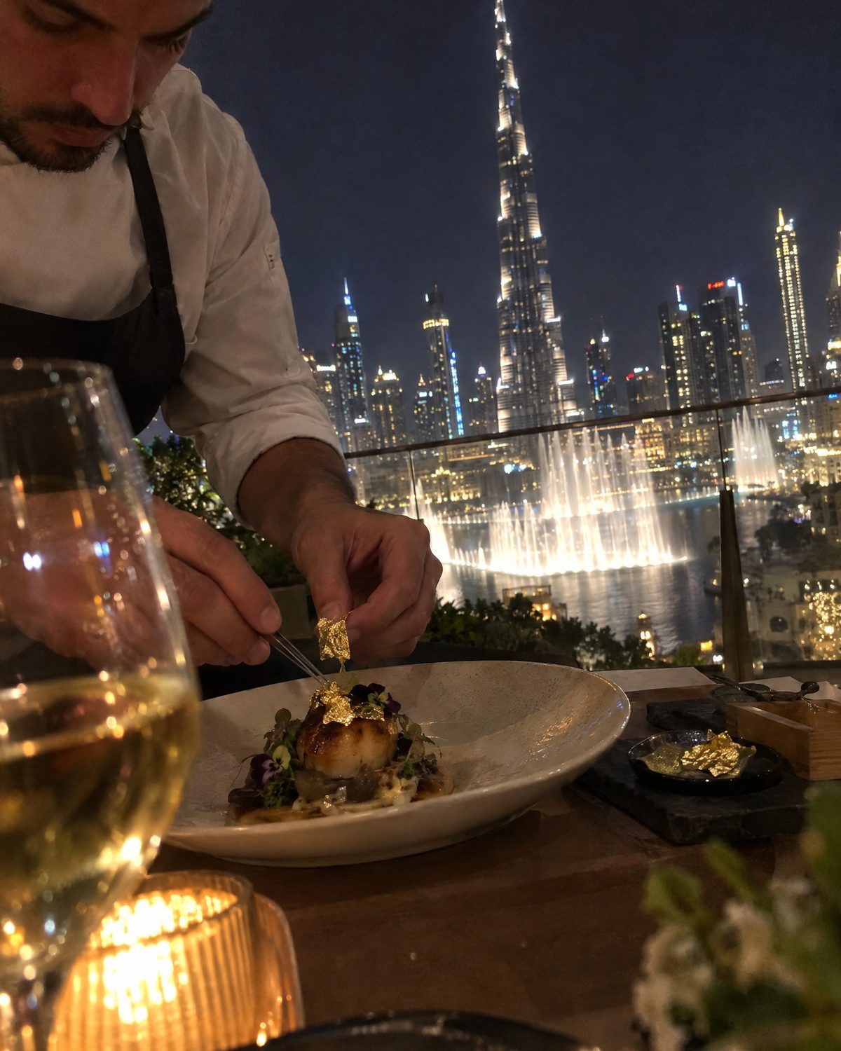 Chef plating with gold leaf on a terrace facing the Burj Khalifa and Dubai Fountain